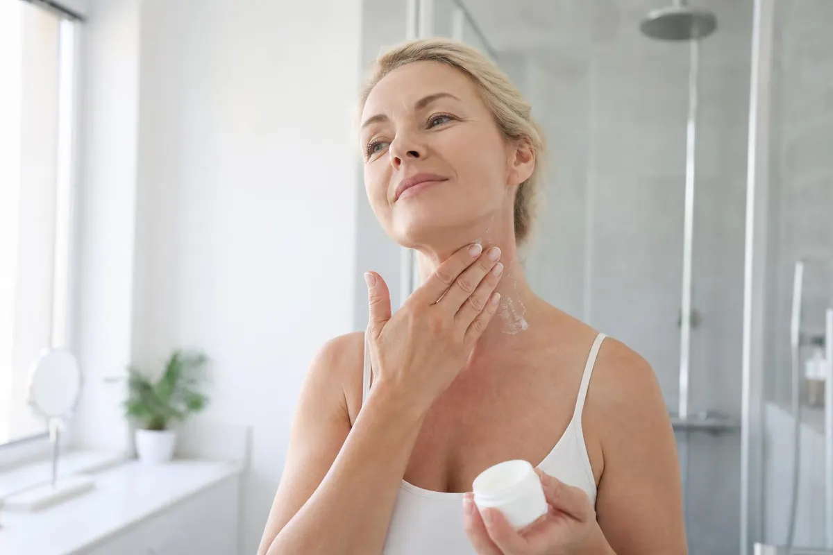 Mujer de unos cincuenta años aplicándose crema en el cuello con movimientos suaves para quitar las arrugas del cuello